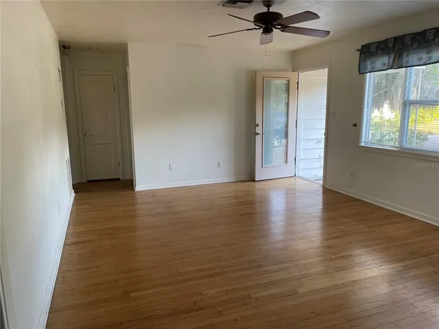 an empty room with wooden floor chandelier fan and windows