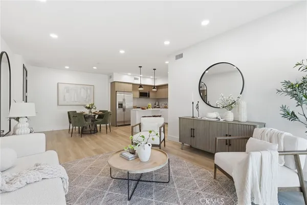 a living room with furniture a mirror kitchen view and a table