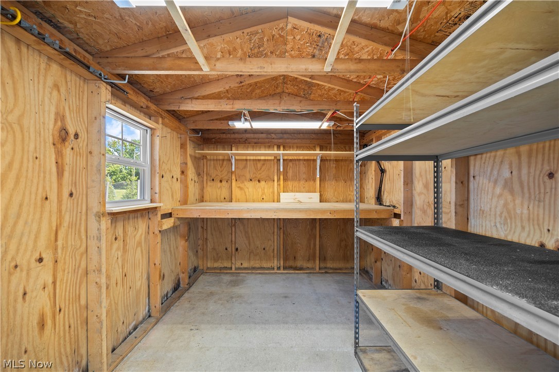35157 Center Ridge Road, Unit 150 North Ridgeville, OH 44039 - Photo 27 of 33 Utility shed interior featuring plywood walls, exposed rafters, concrete flooring, a built-in workbench, and multi-tier metal shelving