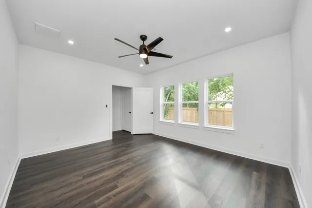 an empty room with wooden floor fan and windows