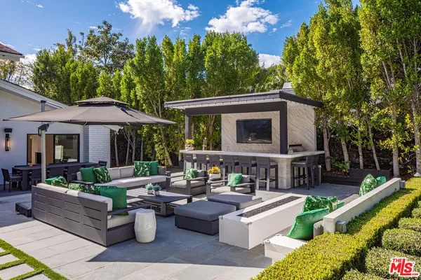 a view of a patio with couches table and chairs under an umbrella with large trees
