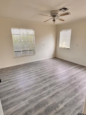 an empty room with wooden floor chandelier fan and windows