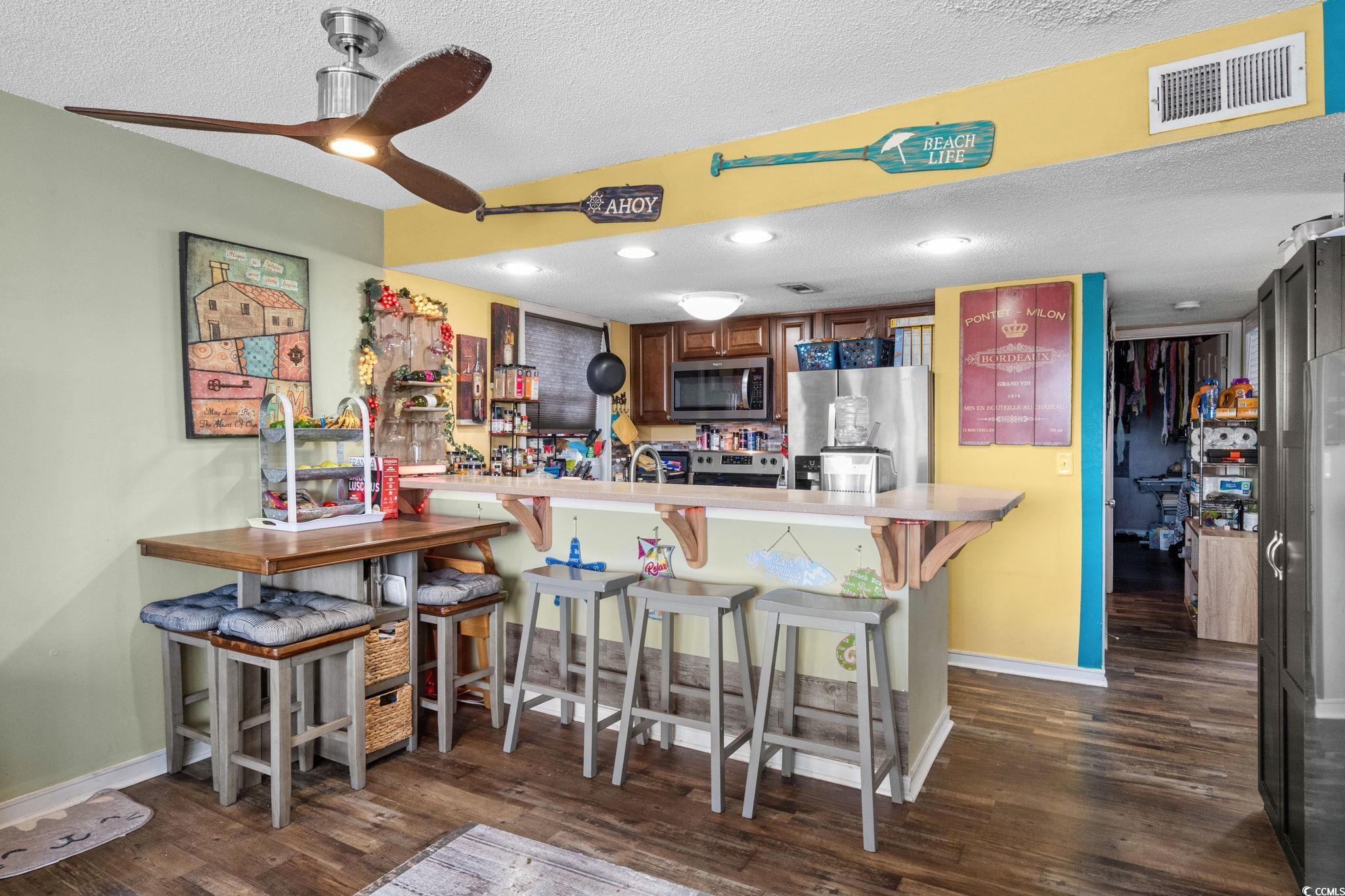 351 Lake Arrowhead Road, Unit 275 Myrtle Beach, SC 29572 - Photo 6 of 37 Kitchen featuring a textured ceiling, light countertops, stainless steel appliances, dark wood-type flooring, and a breakfast bar area