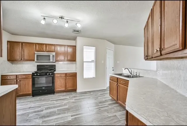 a kitchen with stainless steel appliances granite countertop a stove top oven a sink dishwasher and a refrigerator with wooden cabinets