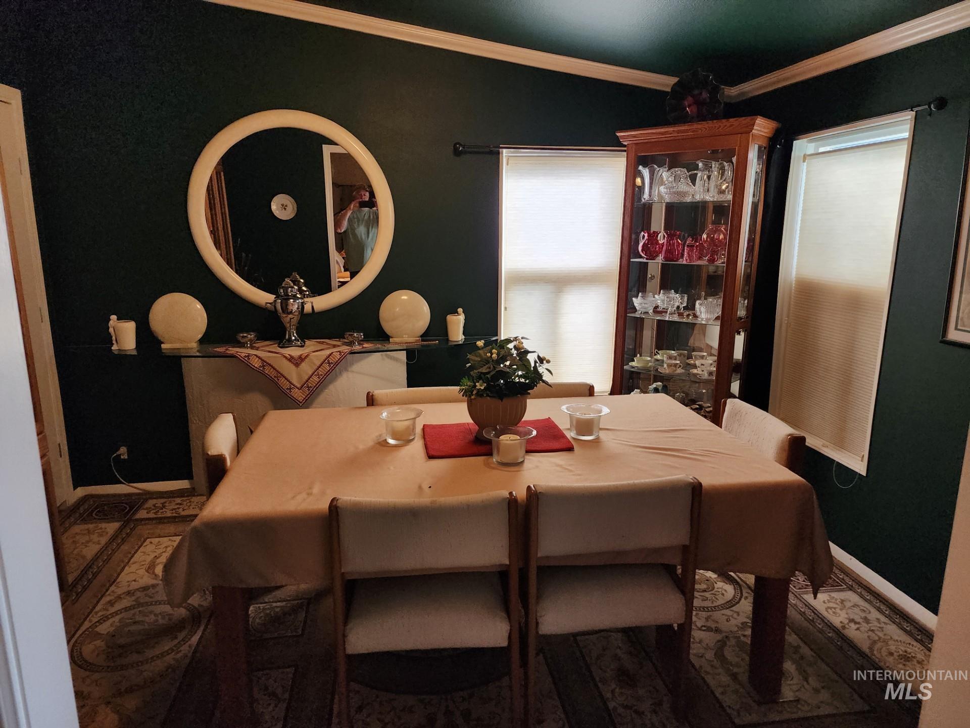 235 5th Street Grand View, ID 83624 - Photo 19 of 22 Dining area featuring dark green walls with white crown molding, a built-in display cabinet with glass doors, and two windows with roller shades