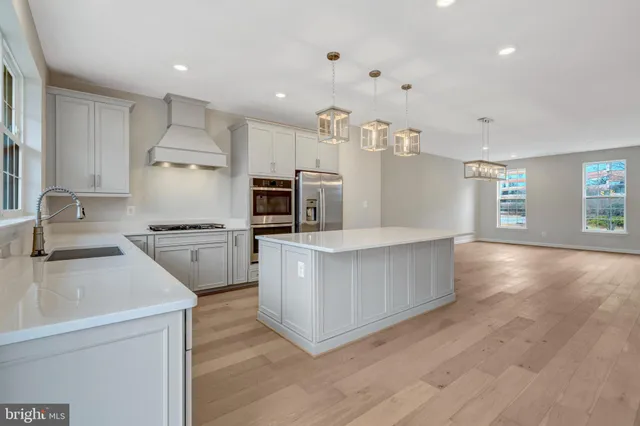 a kitchen with stainless steel appliances a stove top oven a sink dishwasher a refrigerator and white cabinets with wooden floor