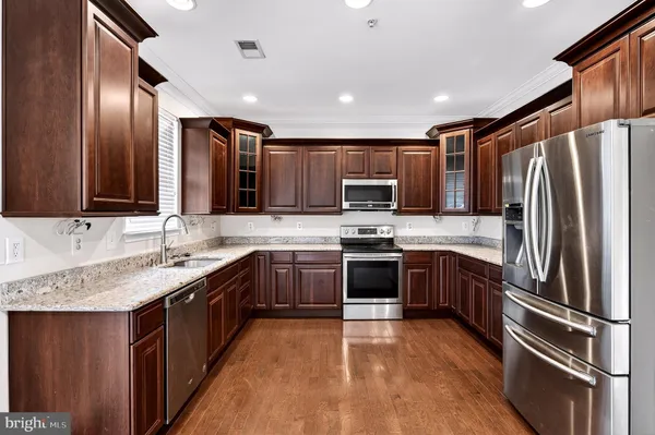 a large kitchen with stainless steel appliances granite countertop a stove a sink dishwasher a refrigerator and a microwave oven with wooden floor