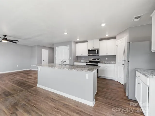 a large kitchen with kitchen island a sink a stove a refrigerator and white cabinets with wooden floor