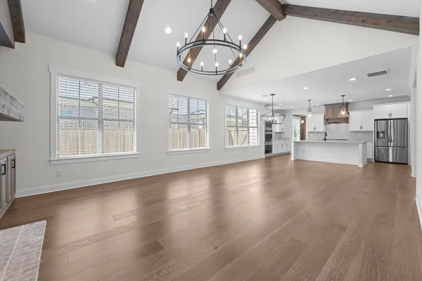 an empty room with wooden floor a kitchen view and windows