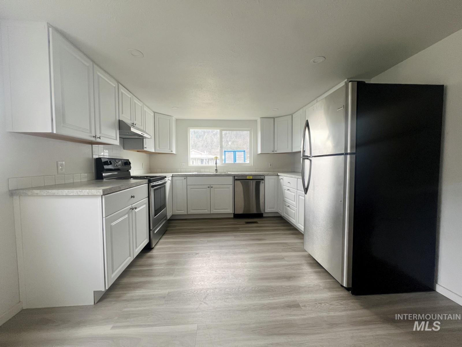 614 Pine Avenue Kooskia, ID 83539 - Photo 7 of 27 Kitchen with stainless steel appliances, white cabinets, light countertops, light wood-style flooring, and under cabinet range hood