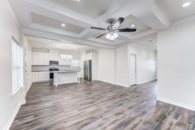 a view of an empty room with wooden floor and a kitchen