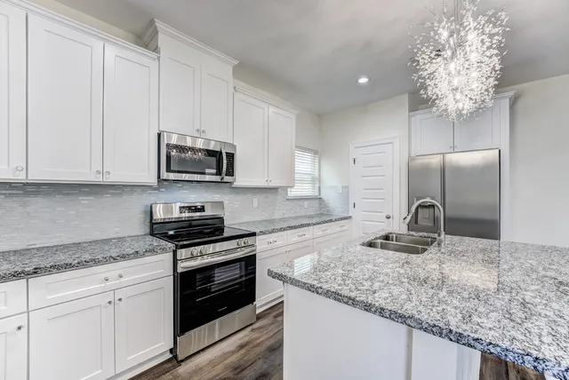 a kitchen with granite countertop a sink dishwasher stove and refrigerator with wooden floor
