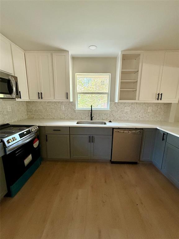 4815 Kelman Street Dallas, TX 75214 - Photo 5 of 16 Kitchen featuring gray cabinets, white cabinets, appliances with stainless steel finishes, light wood-style flooring, and backsplash