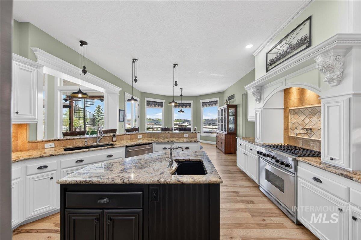 414 East Shafer View Drive Meridian, ID 83642 - Photo 11 of 50 Kitchen featuring hardwood flooring, custom white perimeter cabinetry with dark hardware, and a granite topped center island with an undermount sink & disposal, with black painted storage cabinet with drawers