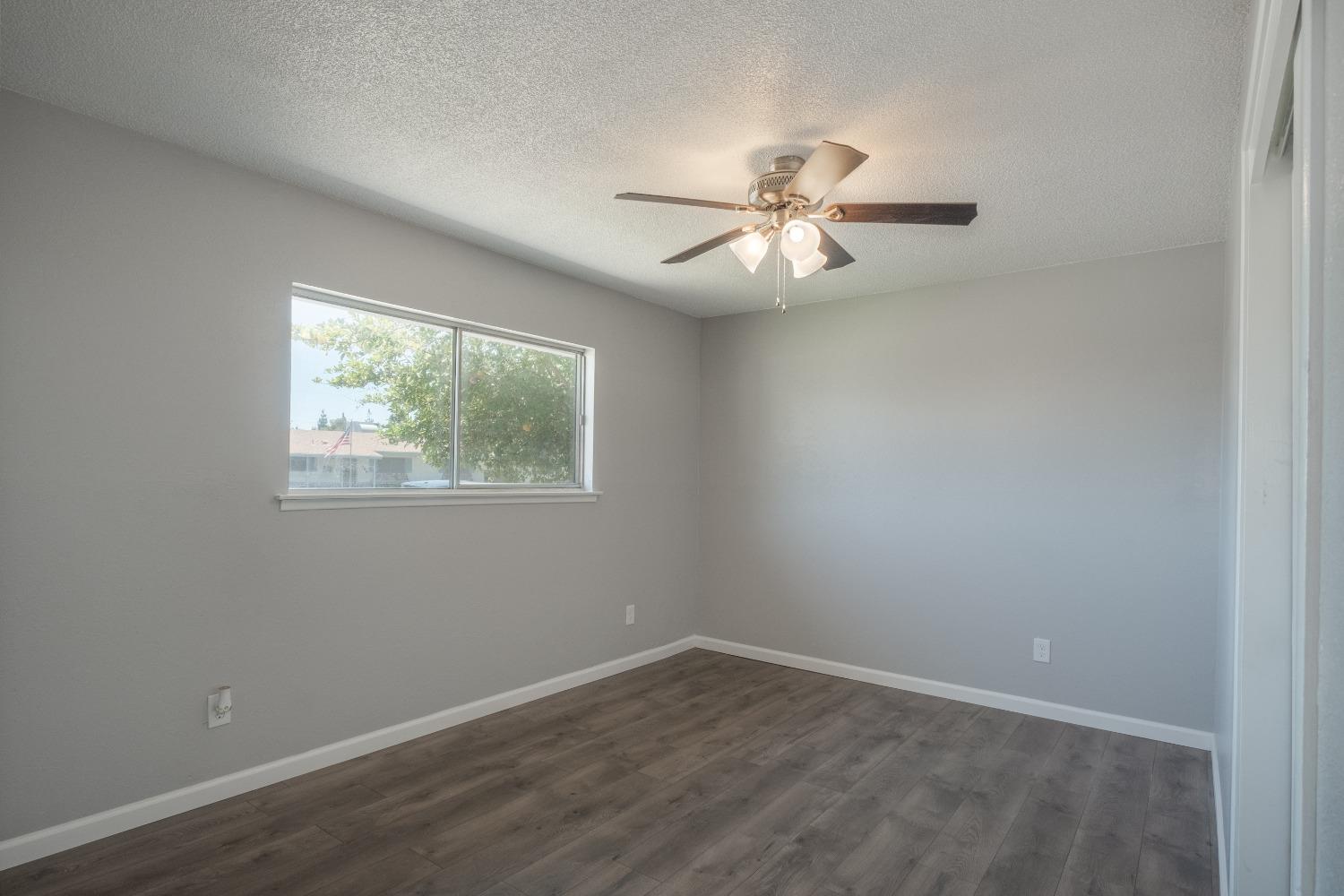 194 West Spring Lane Lemoore, CA 93245 - Photo 9 of 15 an empty room with wooden floor ceiling fan and window