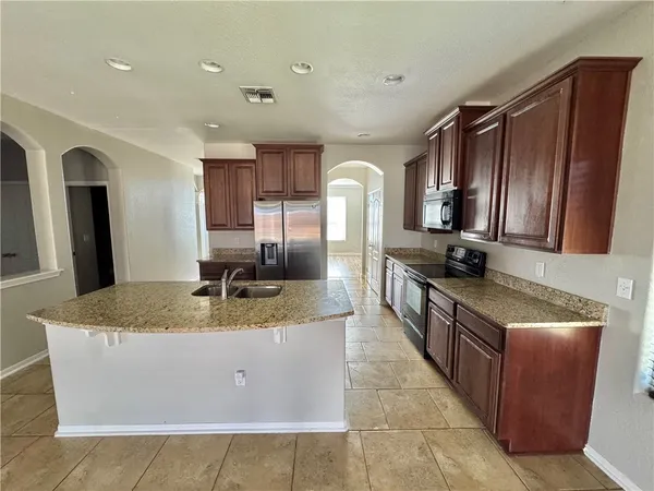 a large kitchen with kitchen island granite countertop a sink refrigerator and cabinets