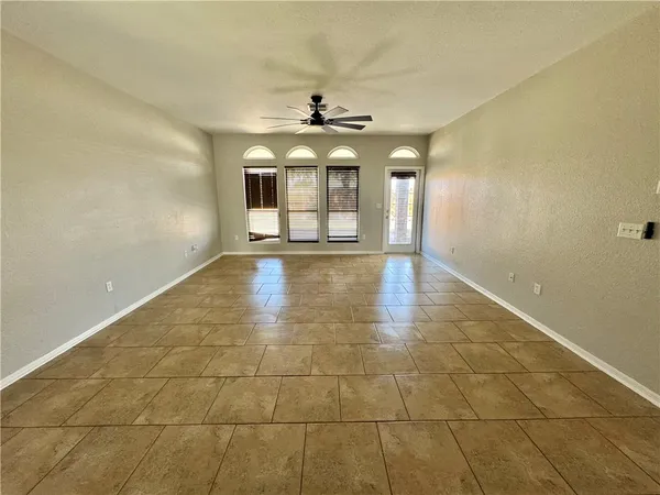 a view of an empty room with chandelier fan and windows