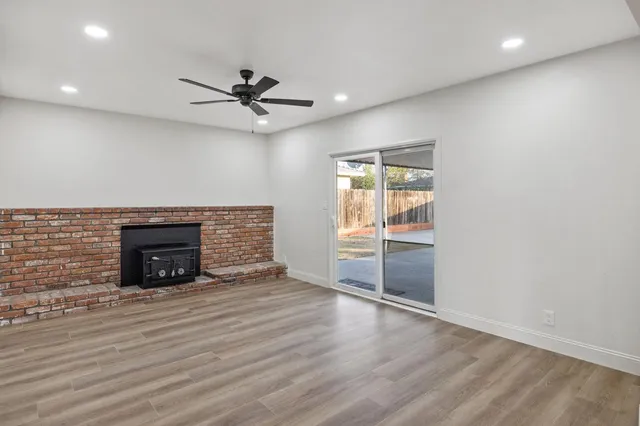 an empty room with wooden floor a ceiling fan a fireplace and windows