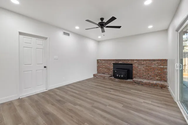a view of an empty room with wooden floor fireplace and a window