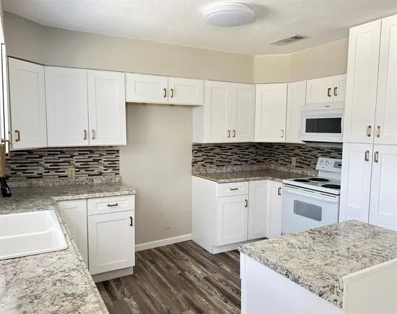 a kitchen with granite countertop a sink stove and white cabinets