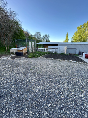 387 North Loafer Canyon Road Payson, UT 84651 - Photo 82 of 94 Gravel driveway leading to a metal-sided outbuilding with a lean-to extension, white fencing, and an established garden bed