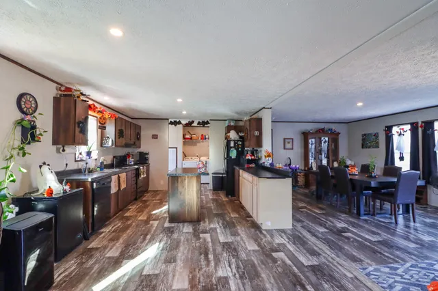 a kitchen with stainless steel appliances granite countertop a refrigerator a sink dishwasher a stove and a dining table with wooden floor