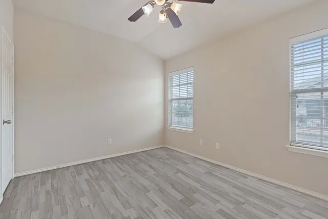 an empty room with wooden floor chandelier fan and windows