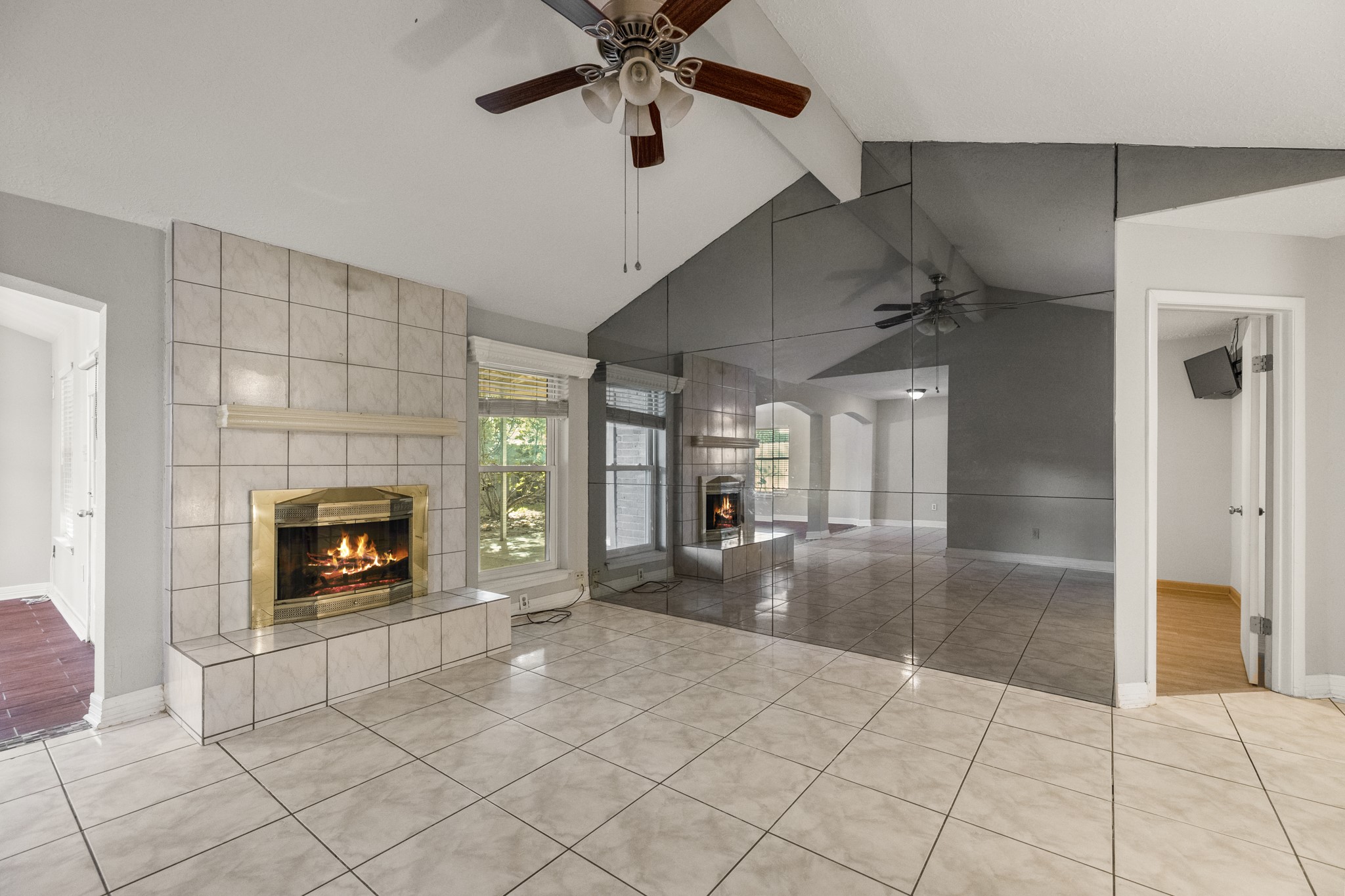 23826 Lestergate Drive Spring, TX 77373 - Photo 14 of 45 Vaulted ceilings give the living room an airy feel, while the tiled fireplace with raised hearth creates a cozy focal point for movie nights, slow mornings, or winding down at the end of the day. Mirrored accent walls bounce natural light through the room and add extra visual depth, with the single window beside the fireplace bringing in even more brightness. Just to the right, the doorway leads into the primary bedroom, keeping the suite close to the home’s main gathering space.