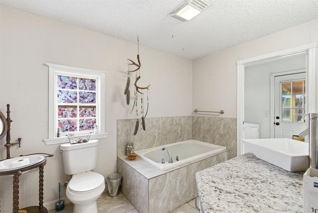 302 Tower Road Rio Vista, TX 76093 - Photo 20 of 29 Bathroom featuring a drop-in bathtub with tiled surround, a white toilet, and a vanity with a rectangular vessel sink and speckled countertop