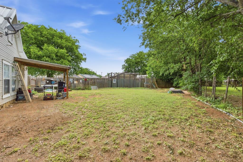 302 Tower Road Rio Vista, TX 76093 - Photo 8 of 29 Expansive backyard featuring a partial wooden privacy fence, mature perimeter trees, and a covered patio area with a slatted wood roof