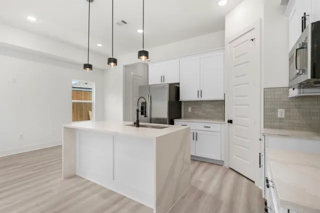 a kitchen with stainless steel appliances granite countertop a refrigerator a oven and white cabinets with wooden floors