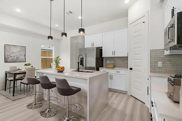 a kitchen with stainless steel appliances kitchen island granite countertop a stove a sink a refrigerator and white cabinets with wooden floor