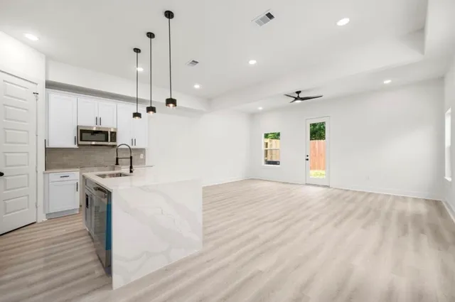 a kitchen with stainless steel appliances kitchen island granite countertop a refrigerator a stove and white cabinets with wooden floor