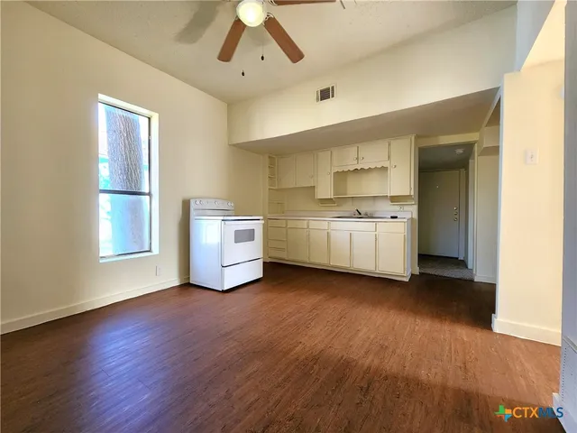 a kitchen with stainless steel appliances a stove a sink and white cabinets with wooden floor next to windows