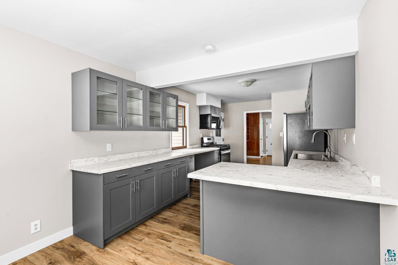 3754 Carlton Street Barnum, MN 55707 - Photo 27 of 52 Kitchen with gray cabinetry, stainless steel appliances, glass insert cabinets, light wood-type flooring, and a peninsula