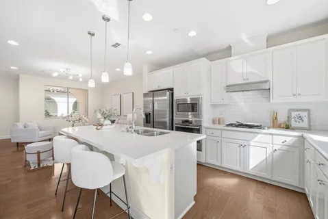 a kitchen with stainless steel appliances kitchen island granite countertop a stove a sink a refrigerator and white cabinets with wooden floor