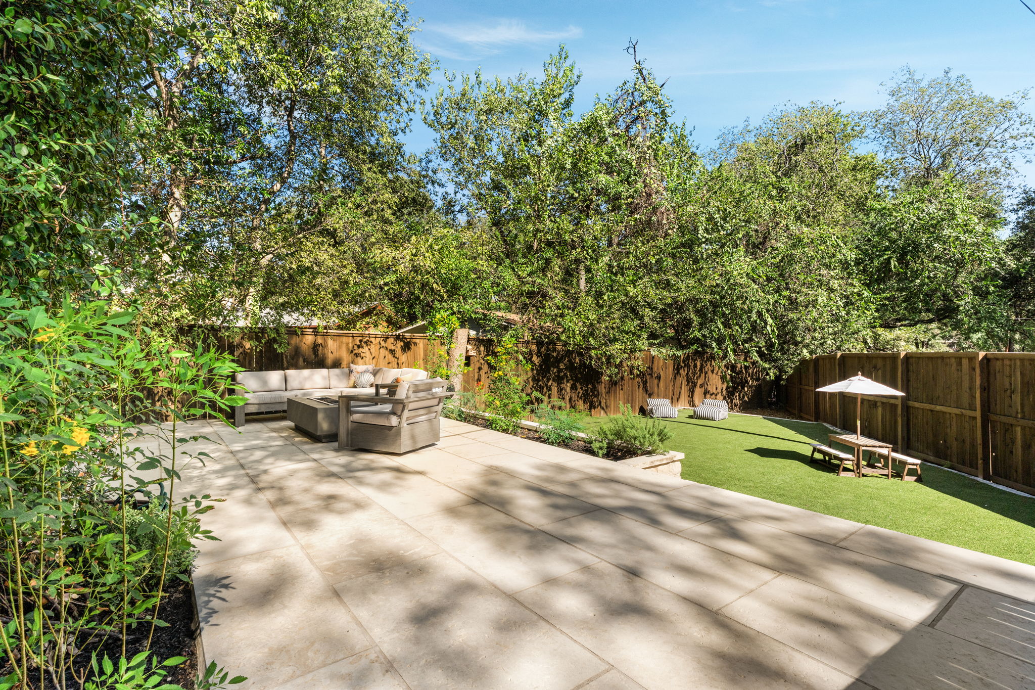 2324 Kinney Road Austin, TX 78704 - Photo 31 of 35 Mature trees frame a spacious stone tile patio bordering a lush lawn and wood privacy fence.