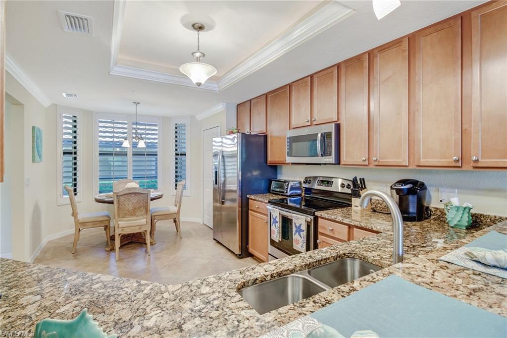 9514 Avellino Way, Unit 2116 Naples, FL 34113 - Photo 10 of 30 a kitchen with stainless steel appliances granite countertop a stove top oven a sink dishwasher a dining table and chairs with wooden floor
