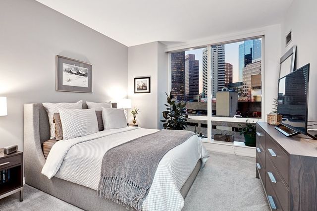 a bedroom with bed a flat tv screen and a large window with the outer view