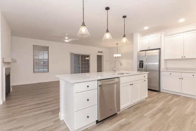 a large kitchen with granite countertop a stove a sink and white cabinets with wooden floor