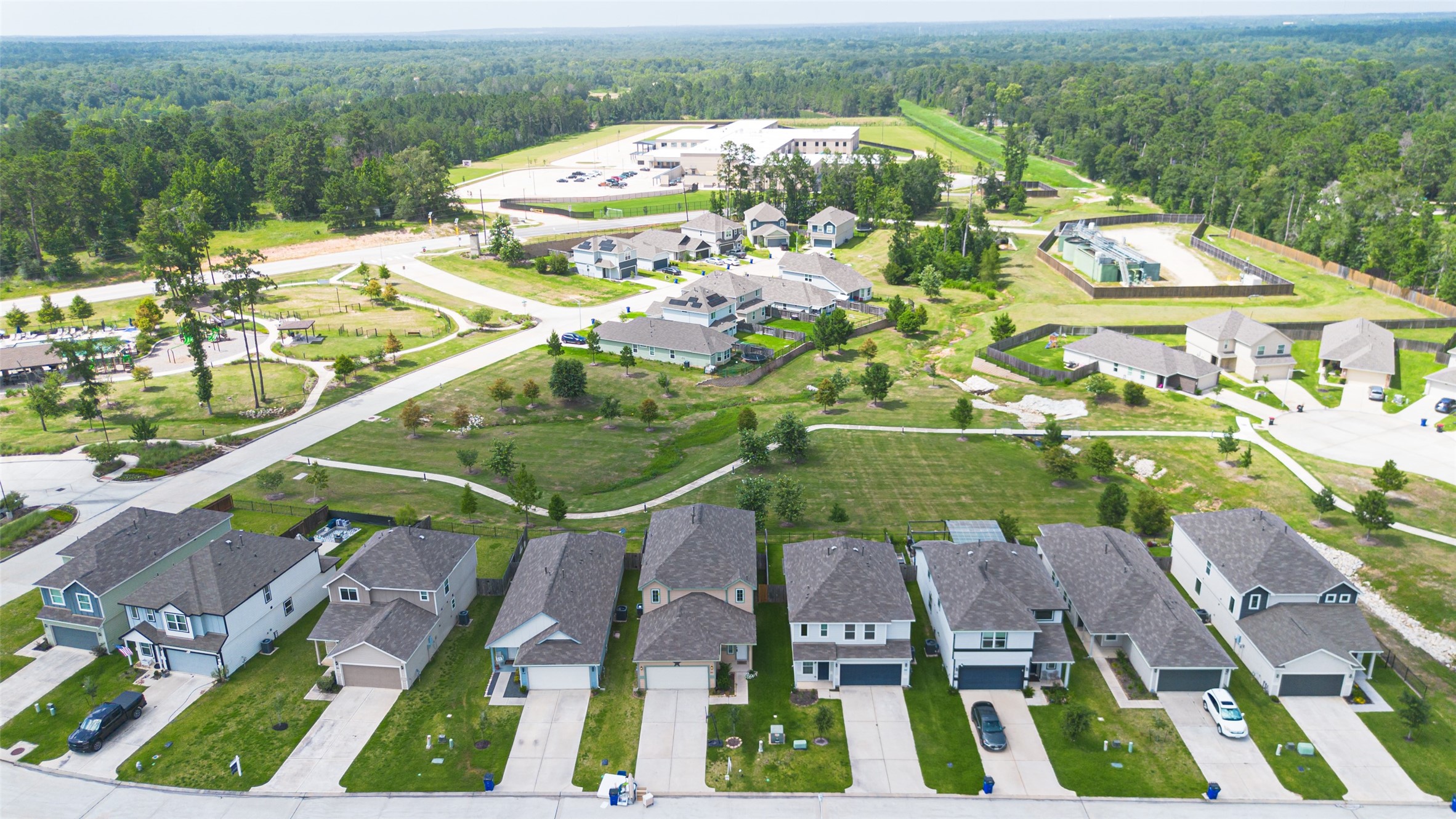 2526 Sturgeon Way Conroe, TX 77384 - Photo 47 of 49 This photo showcases a suburban neighborhood with a row of modern, well-maintained homes. The area features spacious green spaces, a nearby community center, and a pool, all set against a backdrop of lush forest. Ideal for families seeking a peaceful and community-oriented environment.