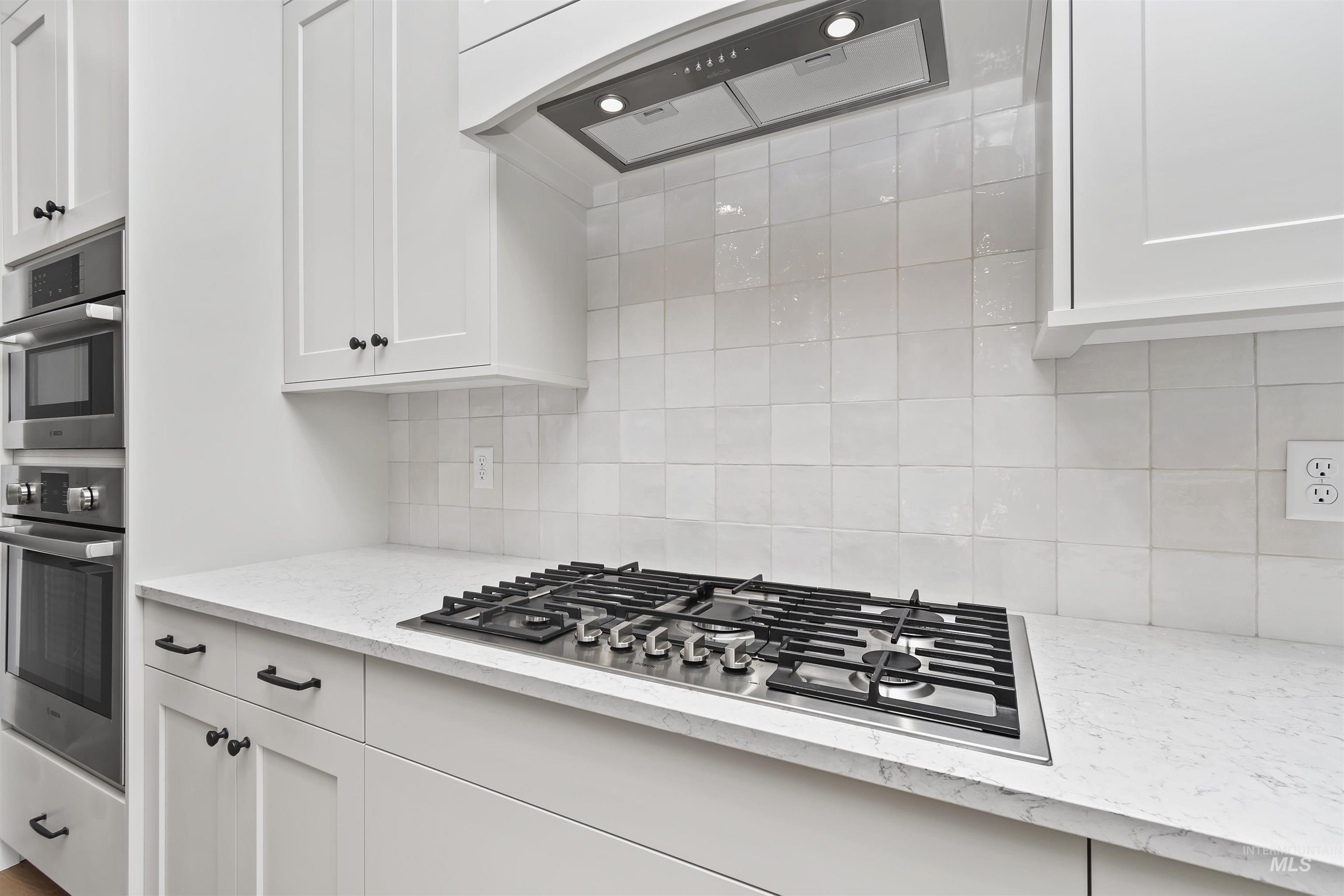 3875 South Corabell Avenue Meridian, ID 83642 - Photo 8 of 27 Kitchen with stainless steel appliances, white cabinetry, light stone counters, exhaust hood, and tasteful backsplash