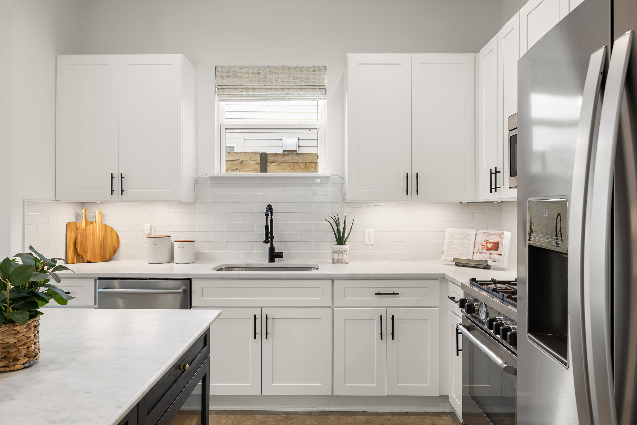 1201 Luna Street Austin, TX 78721 - Photo 11 of 31 Two tone kitchen featuring stainless steel appliances, light stone countertops, tasteful backsplash, and two tone cabinetry
