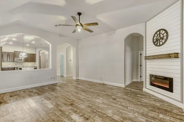 a view of a livingroom with a fireplace a ceiling fan and kitchen view