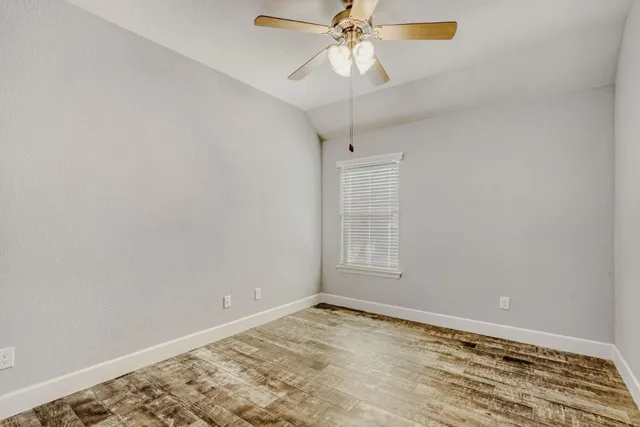 an empty room with wooden floor fan and windows