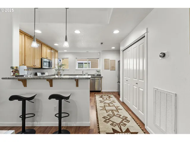 a open kitchen with stainless steel appliances kitchen island granite countertop a refrigerator a stove a sink dishwasher and white cabinets with wooden floor