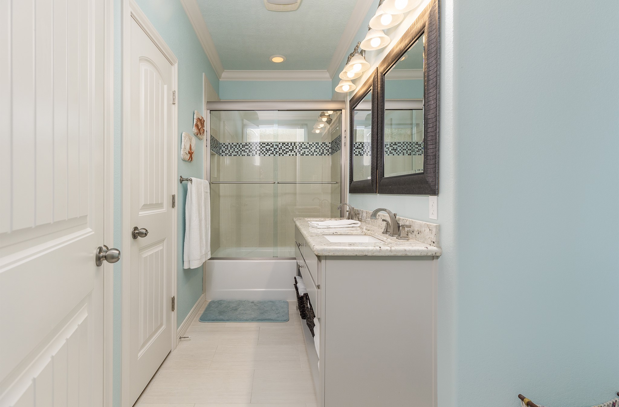 843 South Jacks Road Crystal Beach, TX 77650 - Photo 39 of 45 This bathroom features a clean, modern design with soft blue walls, a double sink vanity with granite countertops, and a large mirror with ample lighting. The shower has a glass door and stylish tile accents, creating a bright and inviting space.