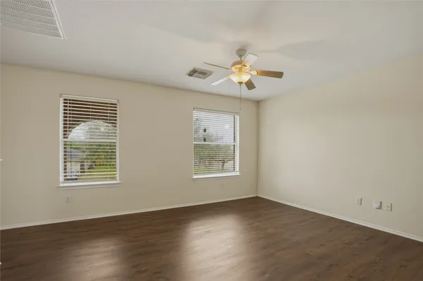an empty room with wooden floor chandelier fan and windows