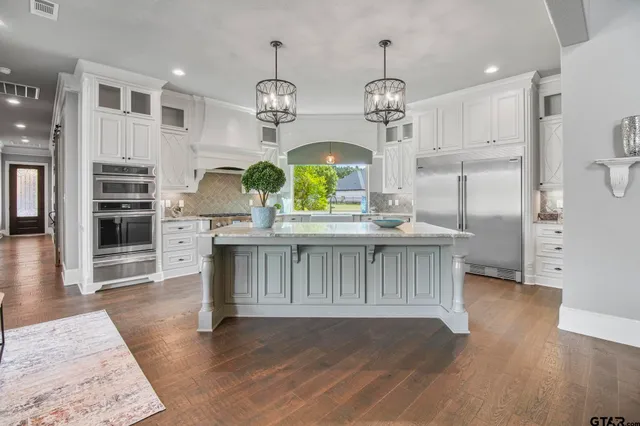 a kitchen with stainless steel appliances granite countertop a refrigerator a sink dishwasher a stove and a dining table with wooden floor