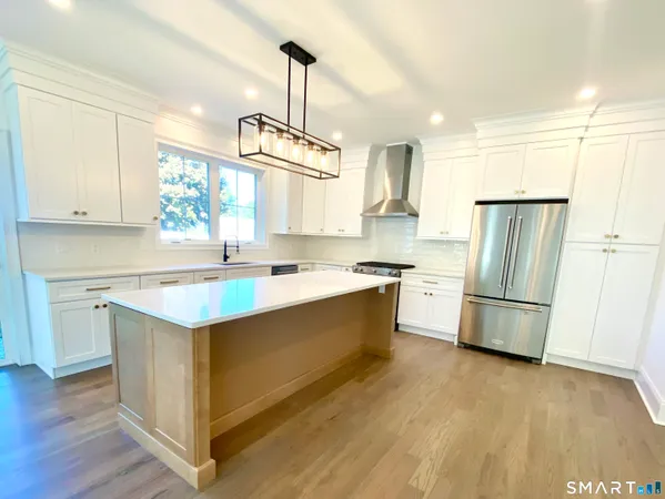 a kitchen with stainless steel appliances granite countertop a refrigerator a sink dishwasher a stove and white countertops with wooden floor